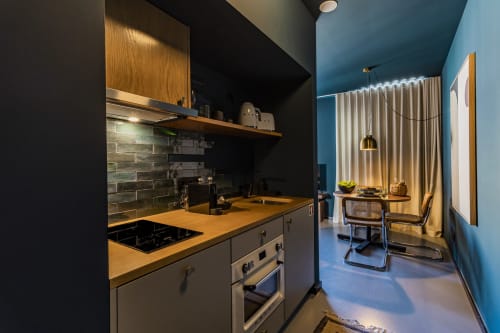 Cozinha compacta moderna em estúdio de hotel no Porto com backsplash em azulejos escuros, bancada de madeira, fogão e área de refeições azul
