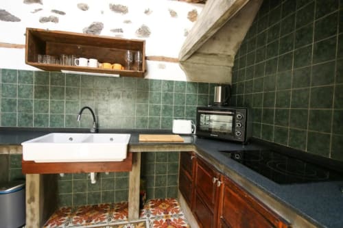 Cocina rústica en Casa 1820 con paredes de azulejos verdes, fregadero blanco, estufa negra, muebles de madera y decoración vintage en Santa