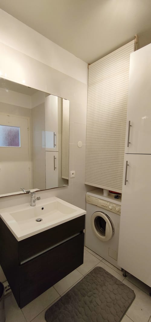 Salle de bain moderne de l'appartement Mer et Maisons à La Trinité sur Mer avec lavabo blanc, miroir, machine à laver et rangements