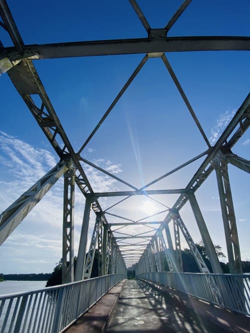 Passerelle métallique enjambant la rivière sous un ciel bleu clair à Sinnamary, Guyane française