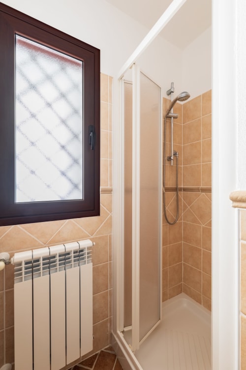 Bagno moderno con doccia a filo pavimento, piastrelle marroni, radiatore e finestra smerigliata nell'appartamento Youinsardinia a Bari Sardo