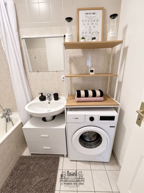 Salle de bain moderne avec combo lave-sèche, lavabo rond, étagères en bois et serviettes rayées à l'appartement Le Paradis Des Logis.
