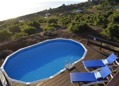 Piscina ovalada azul con tumbonas en terraza de madera con vistas a exuberantes jardines y montañas en Villa Las Flores, Tijarafe