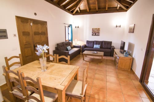 Sala de estar Villa Rodrigo con mesa de comedor de madera, sofás oscuros y piso de terracota en Corralejo