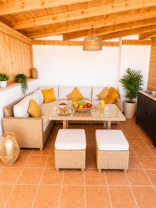 Salon de détente en bois avec sièges en rotin, coussins crème, coussins jaunes et rafraîchissements à Sara & Gino Fuerteventura
