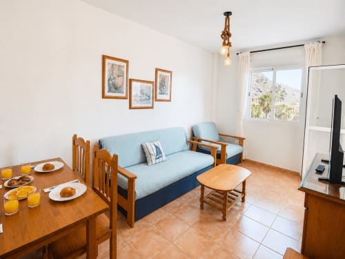 Bright apartment living room with blue sofa, wooden dining table, sea view balcony at Apartamentos El Calón Playa, Cuevas del