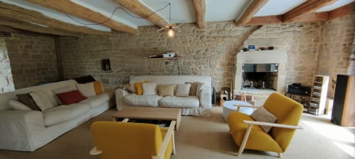 Spacieux salon de villa à Mer et Maisons avec murs en pierre, plafond à poutres, cheminée et fauteuils jaunes