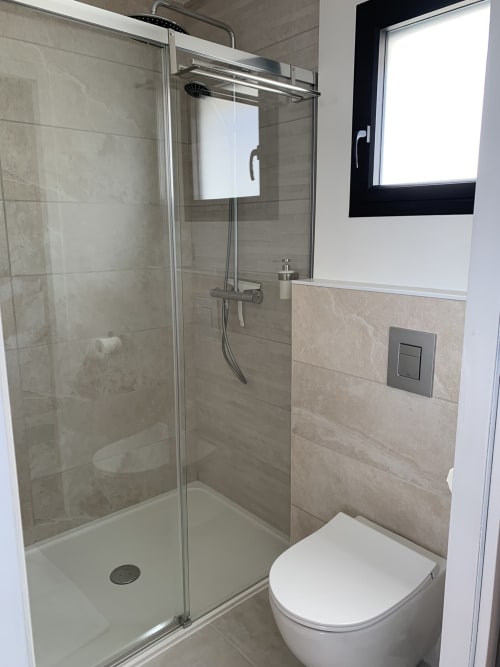 Modern bathroom with walk-in shower, white toilet, and beige tile walls at La Maison Blanche B&B in Bouguenais, France