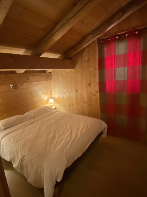 Chambre chaleureuse en bois à La Ferme des Georgières, avec lit, rideaux écossais rouges et charme alpin rustique
