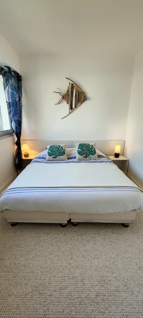 Chambre côtière chez Mer et Maisons avec lit blanc, coussins bleu-vert, décor poisson en bois et accessoires nautiques à La Trinité-sur-Mer