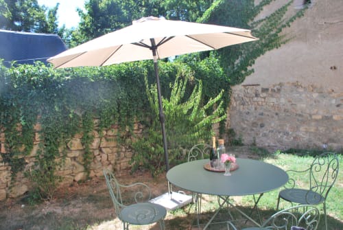 Coin détente ombragé au Château de Vaux Morvan avec parasol, chaises en fer forgé et murs de pierre lierre