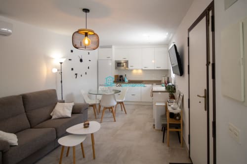 Casa moderna y abierta de estilo Casa. sofá gris, comedor con cocina blanca, luz colgante, reloj de pared, TV y