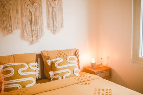 Chambre douillette du gîte ART DE VOYAGER à Étretat avec coussins moutarde, macramés muraux et éclairage chaleureux avec vue