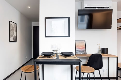 Área de refeições do estúdio moderno do hotel no Porto com mesa preta, cadeiras de madeira, TV na parede e kitchenette