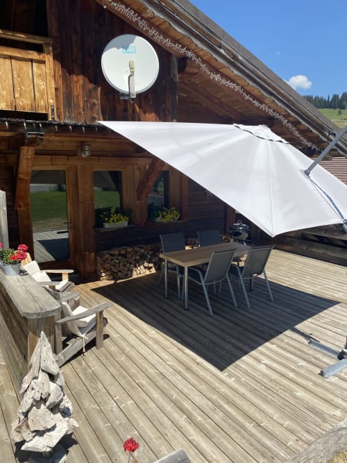 Terrasse rustique en bois avec voile d'ombrage blanc, table à manger et vue sur les Alpes à La Ferme des Georgières