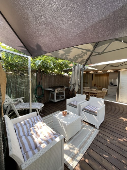 Terrasse extérieure ombragée à La Montagnette, Cap d'Agde avec mobilier en rotin blanc, coussins rayés, coin repas et barbecue