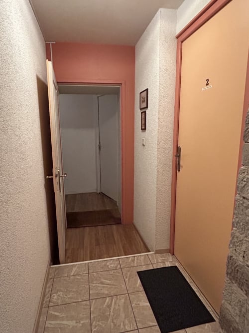 Couloir d'appartement à Hébergement Luxeuil Les Bains avec carrelage, bordures en terre cuite et portes en bois donnant accès aux chambres