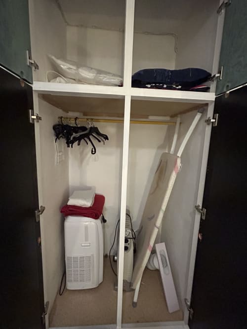 Armoire ouverte dans l'appartement Le Studio à Hébergement Luxeuil Les Bains montrant étagères de rangement, vêtements suspendus et ventilation
