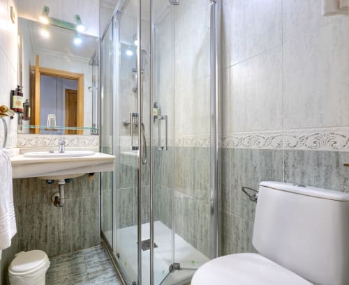 Baño moderno con ducha abierta, lavabo e inodoro en el Hostal El Molino de Collado Villalba