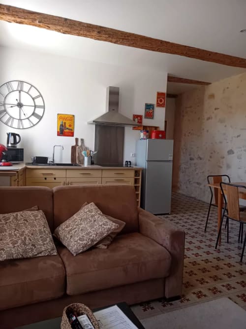 Séjour ouvert du gîte Chez Laure & Marc avec canapé marron, poutres en bois, cuisine et décor vintage à Plaissan