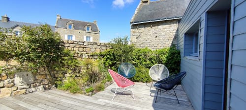 Jardin de villa côtière à Mer et Maisons avec chaises tressées colorées sur terrasse bois, murs en pierre et verdure luxuriante en Laponie.