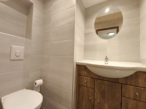 Bagno moderno dello Chalet Coste Belle a Ceillac con piastrelle beige, mobiletto lavabo in legno, specchio rotondo e wc