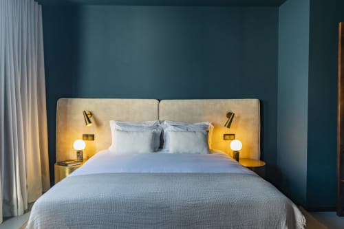 Quarto moderno em hotel no Porto com paredes azul-petróleo, cabeceira bege, roupa de cama branca e iluminação quente das arandelas de latão