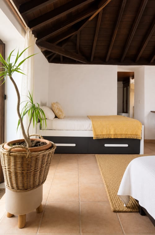 Chambre spacieuse avec lit noir et blanc, poutres en bois, plante en pot et carrelage en terre cuite chez Sara & Gino