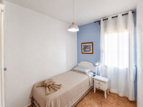 Bright bedroom with blue accent wall, single bed, white nightstand, and sea-view window at Apartamentos El Calón Playa,