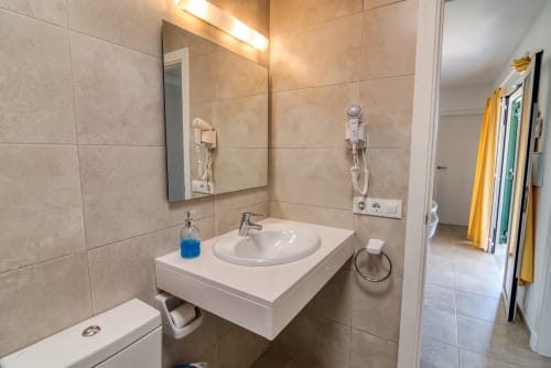 Baño moderno en Las Golondrinas con lavabo blanco, espejo y paredes de azulejos beige, ducha visible a la izquierda