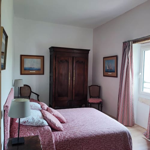 Chambre élégante à la Magnanerie de Sainte Croix avec literie bordeaux, armoire en bois foncé, art nautique et murs roses.