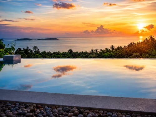 Sunset view from infinity pool overlooking Koh Samui's coast, palm trees, and distant islands at Indigo Villa