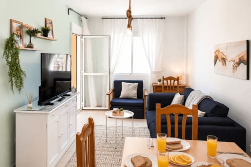 Acogedor interior del apartamento en El Calón Playa con sala de estar, sofá azul marino, sillas de madera y acceso a balcón