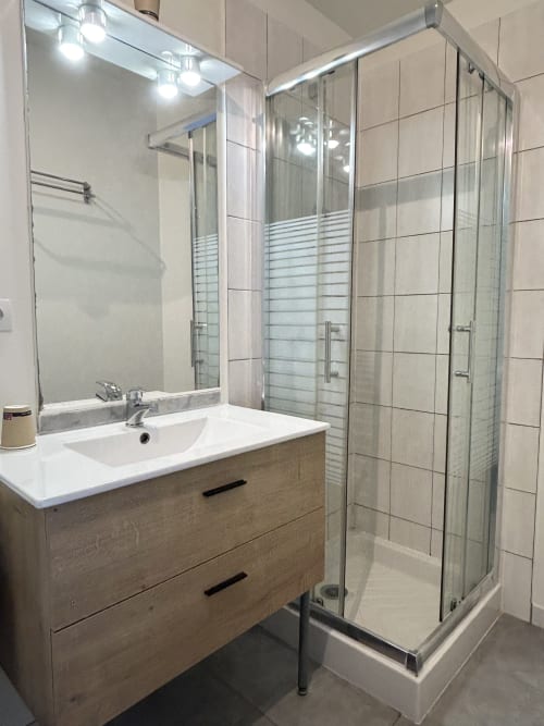 Salle de bain moderne de l'hôtel BDM avec lavabo blanc, meuble vasque en bois, miroir éclairant et douche à l'italienne