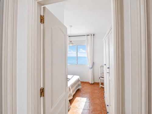 Bright beachfront apartment hallway with sea view through window, terracotta floors, white walls, and bedroom door in Cuevas