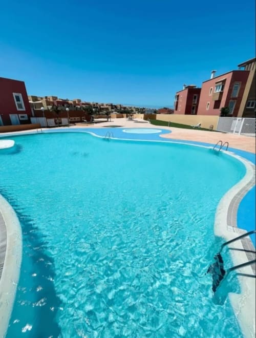 Piscina curva y reluciente del resort Sara & Gino Fuerteventura en Corralejo con apartamentos coloridos y cielo azul despejado