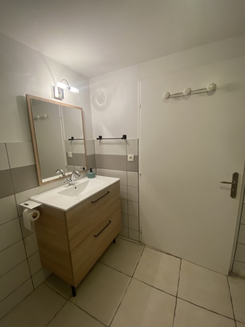 Salle de bain moderne du gîte Le Cocon avec vasque en bois, miroir encadré, douche à l'italienne et carrelage au sol