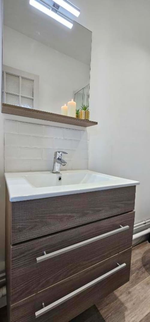 Meuble vasque moderne avec tiroirs en bois foncé, lavabo blanc, robinetterie chromée et miroir rétroéclairé au L'Atelier duplex