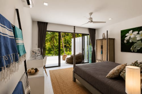 Spacious master bedroom with four-poster bed, ocean views, ceiling fan, and direct access to tropical garden patio at Indigo