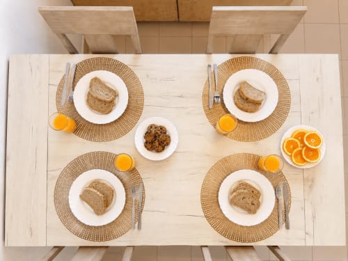 Mesa de desayuno para cuatro personas en Apartamentos El Calón Playa con pan, jugo de naranja y rodajas de cítricos