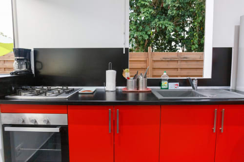 Cuisine moderne rouge du gîte Kaz A Bibi à Sainte-Rose avec plan de travail noir, cuisinière à gaz et vue sur le jardin