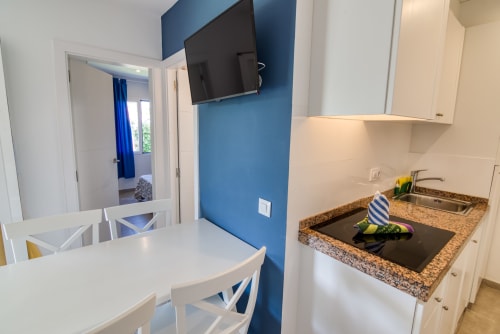 Moderna cocineta con encimeras de granito, TV de pantalla plana en pared azul, área de comedor en Las Golondrinas
