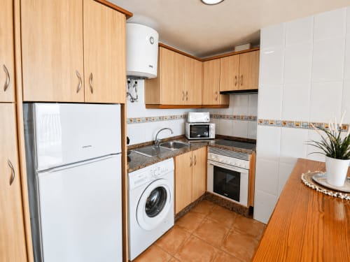 Modern kitchen with wooden cabinets, stainless steel appliances, and tiled backsplash in Apartamentos El Calón Playa