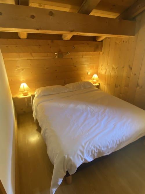 Chambre en bois douillette à La Ferme des Georgières avec lit queen-size, draps blancs et lampes de chevet chaleureuses