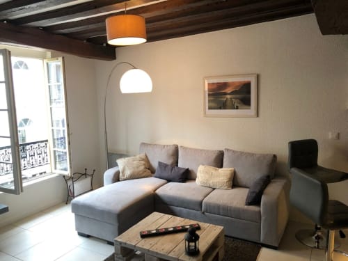Salon d'un appartement parisien moderne avec canapé gris, lampadaire arc, poutres en bois et vue sur la ville au Paillot de