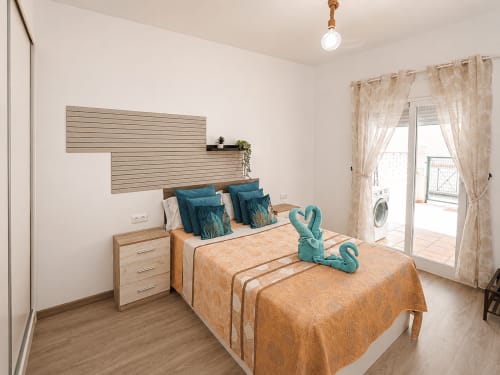 Dormitorio luminoso en Apartamentos El Calón Playa con dos camas, almohadas turquesas, cabecero de madera y acceso a terraza.