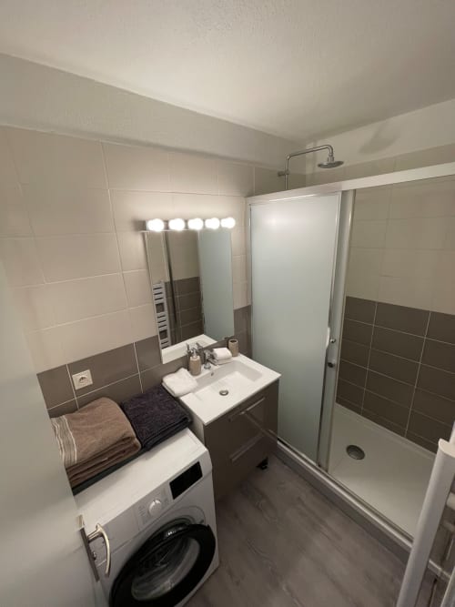 Salle de bain moderne de l'appartement Le Paillot de Montabert à Troyes : lavabo, miroir éclairé, douche, lave-linge et carrelage sombre