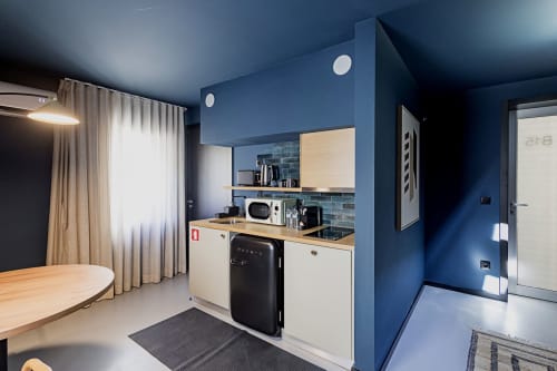 Estúdio moderno do hotel Porto B15 com paredes azuis, kitchenete, mesa de madeira e móveis contemporâneos