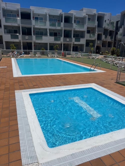 Two swimming pools at FTV Holidays Homes apartment complex in Corralejo with terracotta deck and modern white buildings