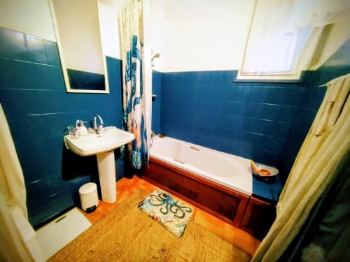 Bathroom with blue tile walls, pedestal sink, bathtub with red trim, and orange floor in French villa